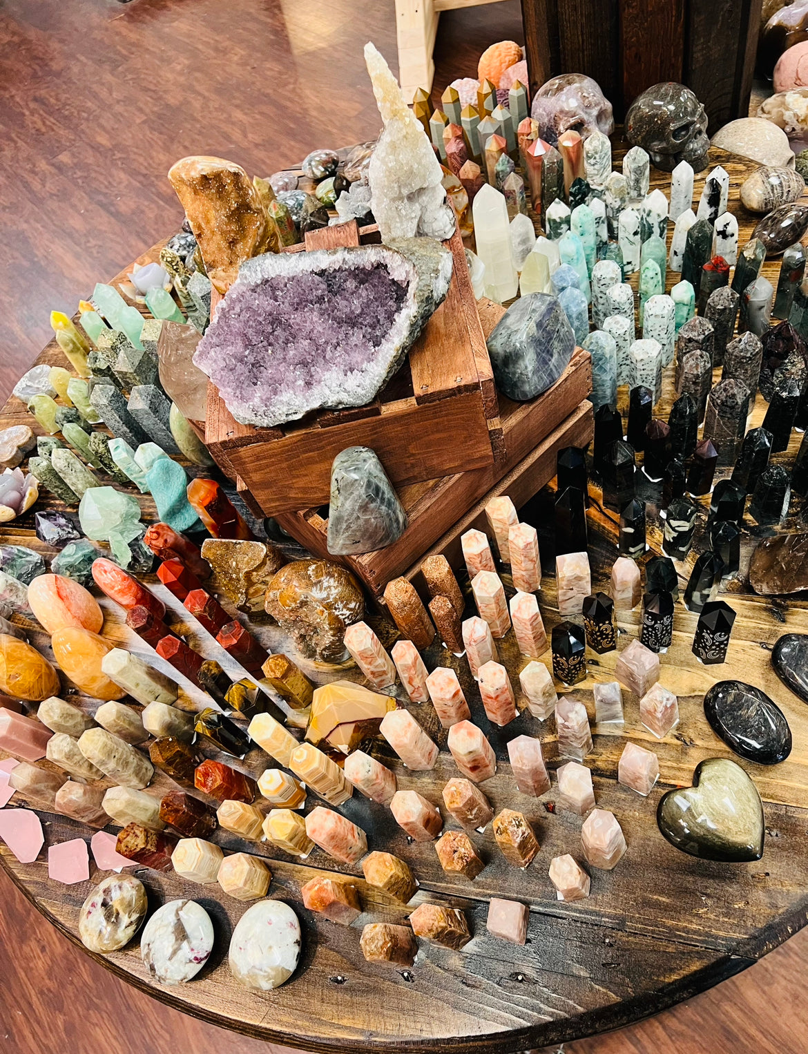 A large collection of various crystals sitting on a table including a large amethyst cluster, carnelian towers, obsidian towers, gold sheen obsidian heart, flower agate eggs, crystal skulls and more