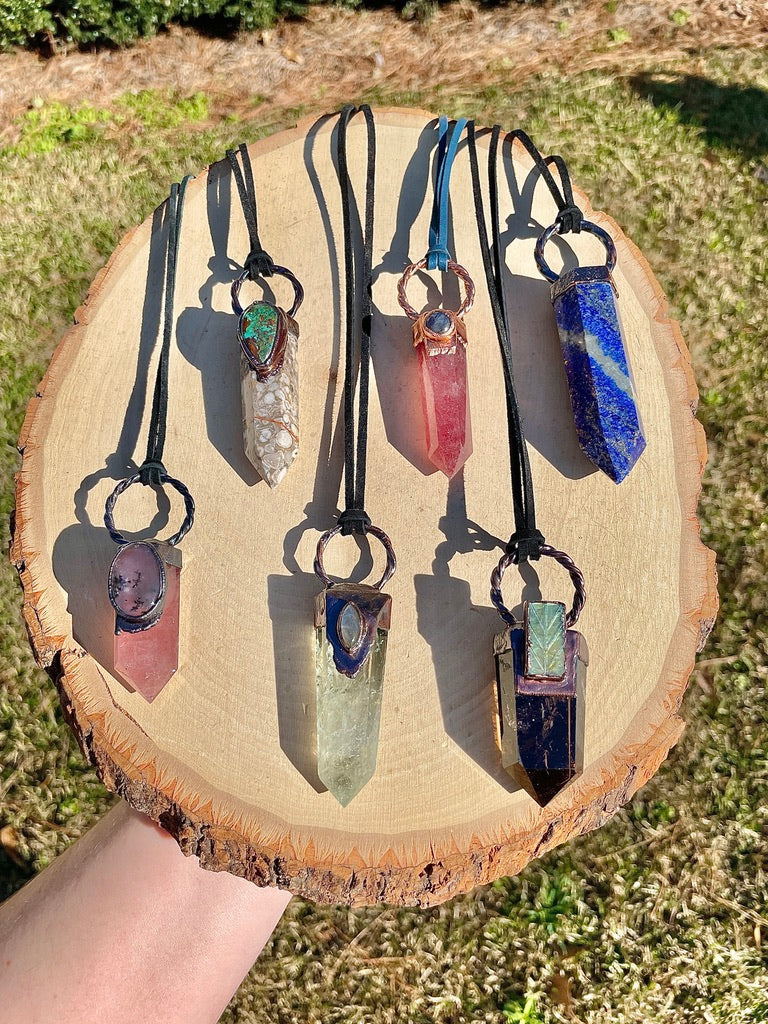 A display of crystal tower pendant necklaces consisting of pink and green quartz, sodalite, flower agate, and obsidian